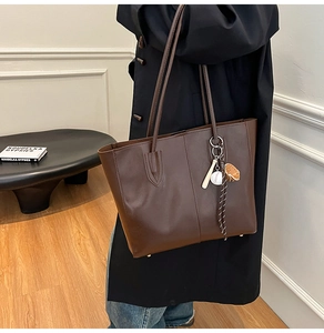 Detail of dark brown leather tote bag with a baseball charm and spacious interior
