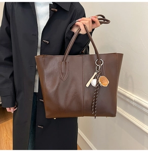 Close-up of vintage brown leather tote bag with creative baseball glove and bat charm
