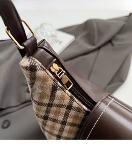 Detail of smooth gold metal zipper on brown leather and checkered fabric tote bag