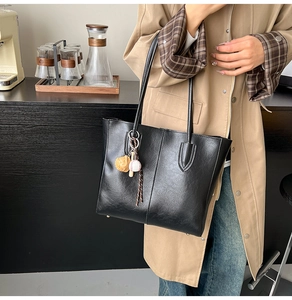 Detail of black leather tote bag with baseball bear charm and gold feet accents