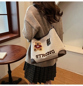 Detail of beige canvas tote bag featuring brown trim and embroidered cartoon bear patch