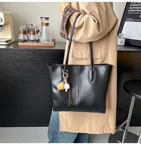 Detail of a black leather tote bag with a baseball charm and long shoulder straps