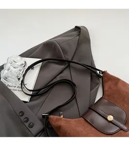 Détail d'un sac bandoulière marron mat vintage avec fermoir doré sur blazer gris