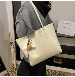 Detail of off-white lychee leather tote bag featuring a baseball glove charm and large space