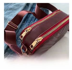 Close-up of wine red crossbody bag with V-shaped quilting and dual golden zippers