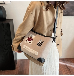 Detail of beige canvas tote with cartoon bear embroidery and black leather trim accents