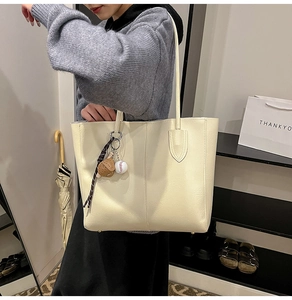 Detail view of cream white tote bag with baseball charm on model in outdoor setting