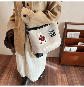 Detail of cream canvas bag with teddy bear embroidery and black leather corner guards