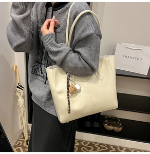 Detail of cream leather tote bag featuring a stylish baseball-shaped leather charm