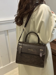 Sacoche vintage marron avec lettrage doré portée par un mannequin en manteau vert