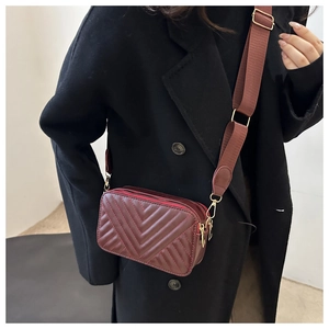 Detail of burgundy quilted crossbody bag with V-shaped stitching and wide textile strap