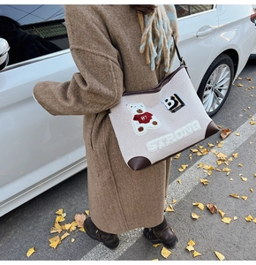 Outdoor lifestyle shot of a beige canvas tote bag with bear patch and leather trim detail