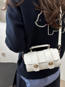 White floral embossed crossbody bag with gold clasps shown on person for style