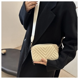 Detail of cream chevron quilted crossbody bag with wide strap and gold hardware