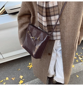 Close-up of gloss leather crossbody bucket bag with gold buckle on autumn street setting
