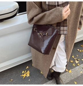 Close-up of glossy dark brown leather bucket bag with metallic buckle on an autumn street