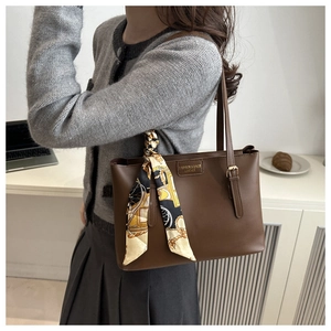Detail of a brown leather tote bag featuring a decorative silk scarf and metal brand plate