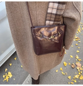 Detail of dark brown glossy leather crossbody bag with vintage metal buckle and strap