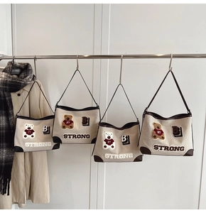 Close-up of four canvas tote bags with bear patches and leather trim on a metal rack