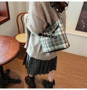 Detail of wool plaid bucket bag featuring leather straps and vintage metallic buckle