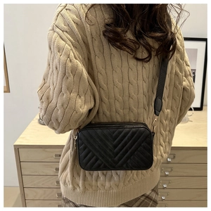 Detail of black V-quilted crossbody bag with gold zippers worn on beige knitted sweater
