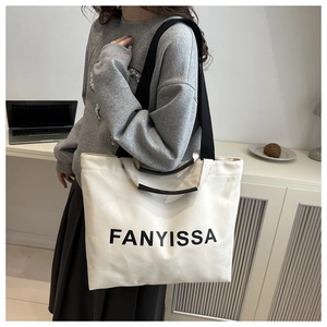 Détail du grand sac cabas en toile crème avec des anses noires et une bandoulière