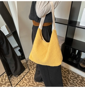 Close-up of fluffy yellow faux fur hobo tote bag with off-white shoulder strap worn by model