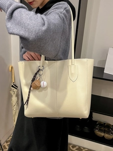 Minimalist beige faux leather tote bag with baseball pendant shown on shoulder