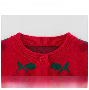 Detail of red knit cardigan featuring cherry jacquard pattern and ribbed crew neck design