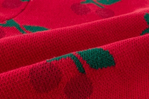 Macro detail of red knitted fabric with soft texture and green leaf embroidery