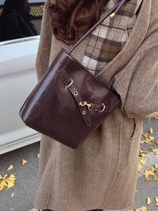 Vintage burgundy leather bucket bag with gold hardware shown in a scenic autumn street setting