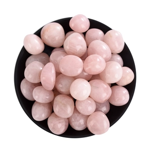Polished natural rose quartz tumbled stones displayed in a minimalist black ceramic bowl