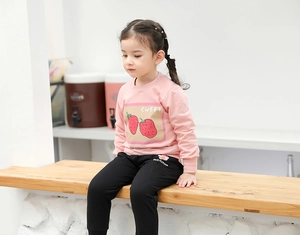 Détail du sweat à fraises rose et du pantalon noir sur un modèle de fille