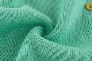 Macro detail of mint green knit fabric with matching round button on child cardigan