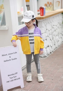 Outdoor shot of a kids' purple and yellow contrast zip-up jacket with a cozy cafe backdrop