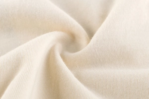 Gros plan sur un tissu en maille crème montrant la texture douce du coton et des coutures