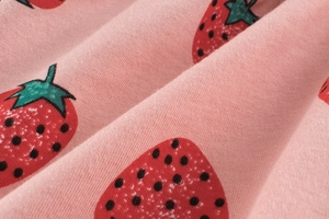 Close-up of soft pink cotton fabric featuring a vibrant red strawberry print pattern