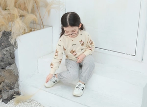 Toddler girl set featuring a beige bear print sweatshirt and grey joggers on a warm backdrop