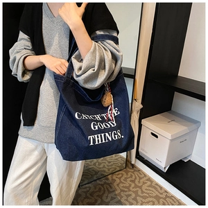 Close-up of a large navy denim tote bag with white text print and a cute bear charm