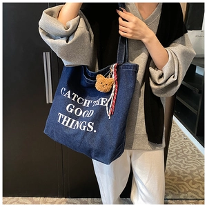 Blue denim tote bag with plush bear charm and white slogan detail for casual style