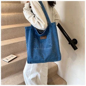 Detail of blue denim tote bag with brown leather patch on strap, casual shoulder style