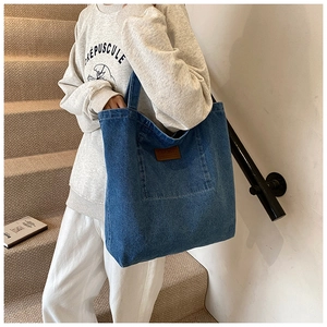 Dettaglio borsa tote in denim blu con pratica tasca esterna e targhetta in pelle
