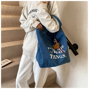 Dettaglio della borsa tote in denim blu con stampa bianca e ciondolo a forma di orso