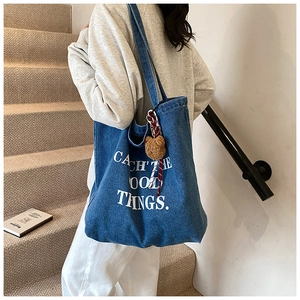 Detail of blue denim tote bag featuring 'CATCH THE GOOD THINGS' print and plush charm