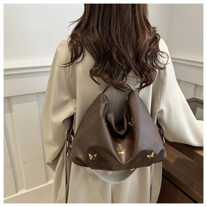 Detail of a brown leather cloud tote with golden butterfly charms on a white coat