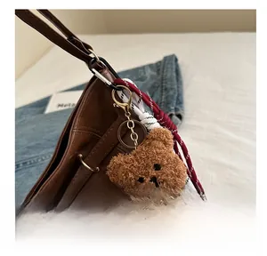 Brown teddy bear plush keychain charm with gold clasp attached to a leather bag