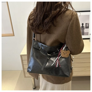 Detail of black faux leather tote bag with metallic buckle and decorative bear charm