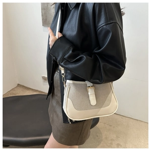 Detail of a minimalist cream canvas saddle bag with white leather trim on a model