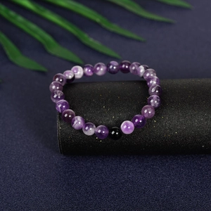 Purple amethyst beaded bracelet with single black accent bead on dark display pedestal