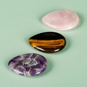 Polished natural aventurine, tiger eye, and amethyst worry stones on a green background